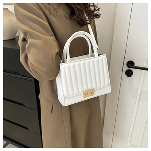 Close-up of white quilted crossbody bag with golden metal buckle and vertical stitching