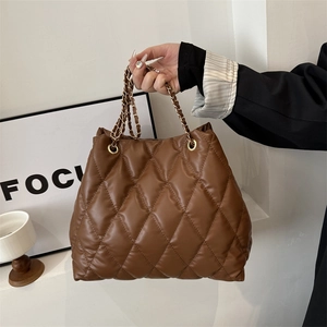 Brown quilted rhombus pattern tote bag with gold chain strap in a minimalist setting