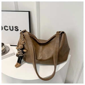 Detail of dark brown pleated tote bag with a plush rabbit charm on a white stand