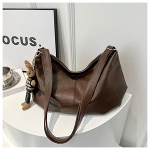 Detail of dark brown pleated crossbody bag with a cute plush rabbit charm on a pedestal