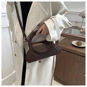 Detail of deep brown geometric handbag with oversized round handle and sleek crossbody strap