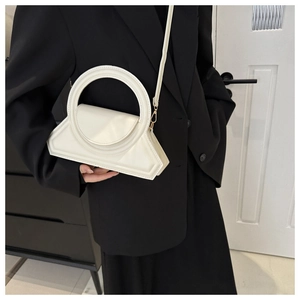 Close-up van witte PU-handtas met rond handvat gedragen over een zwarte blazer voor dames