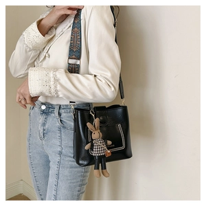 Detail of black pebbled leather crossbody bag with ethnic strap and bunny charm
