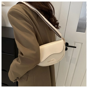 Détail d'un sac selle beige avec bandoulière large et quincaillerie dorée polie