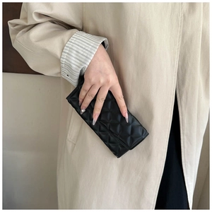 Detailed view of women's black quilted clutch bag held against a beige coat