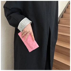 Detail of pink quilted stitch clutch bag held by model wearing a long black coat