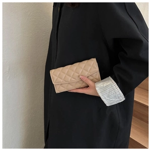 Detail of a beige quilted envelope clutch held against a dark coat for contrast