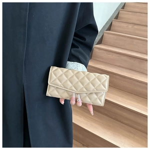 Détail d'une pochette longue en cuir matelassé beige avec grand rabat tenue par un mannequin