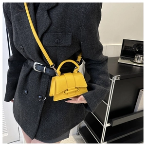 Close-up of a bright yellow mini handbag with litchi texture on a grey blazer outfit