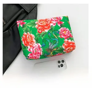 Confronto dimensioni borsa verde con motivo peonia accanto a uno smartphone