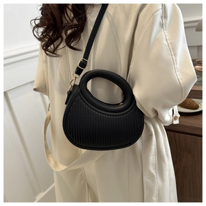 Detail of black pleated crescent handbag with round cutout handle and gold hardware