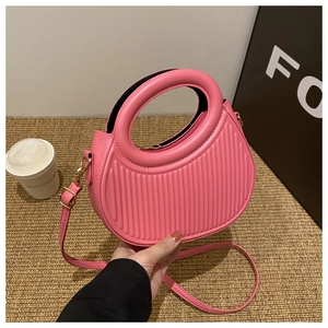 Detailed view of pink pleated crescent handbag with round handle on a woven background