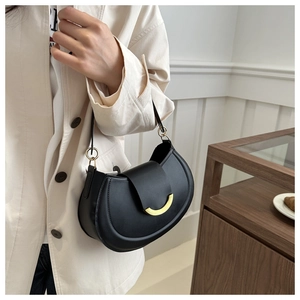 Detail of a black half-moon shoulder bag with a crescent-shaped gold metal buckle closure