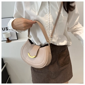 Model wearing a beige saddle bag with gold crescent buckle and adjustable strap