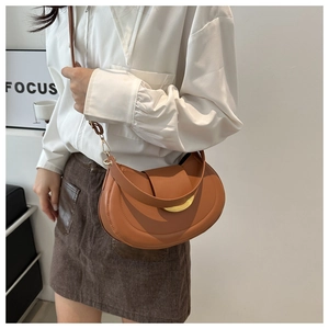 Detail of caramel brown saddle bag featuring a gold semi-circle metal clasp and fine stitching