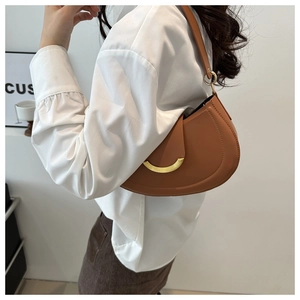Detail of a brown leather half-moon shoulder bag with a gold metal clasp worn by a model