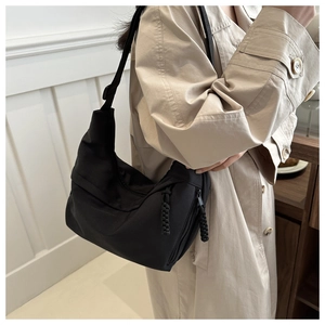 Side view of black matte nylon hobo bag with wide strap on model in minimalist interior