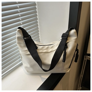 Detail of off-white canvas crossbody bag with adjustable wide black shoulder strap and knot zipper