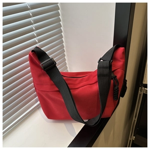 Detail of red crescent shoulder bag with black adjustable strap on a minimalist window sill