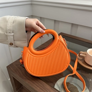 Chic orange half-moon handbag with a round cutout handle and elegant pleated texture