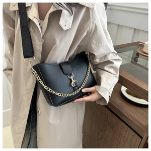 Detail of black semi-circular bucket bag with wide nylon strap and gold chain accent
