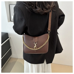 Detail of dark brown leather crossbody bag featuring gold chain and wide woven strap