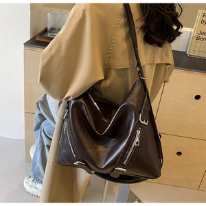 Close-up of dark brown leather tote bag showing side silver zippers and adjustable strap