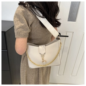 Close-up of beige crescent shoulder bag featuring a wide fabric strap and gold chain detail