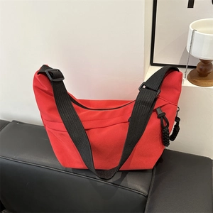 Minimalist red crescent shoulder bag with adjustable black strap on a leather sofa
