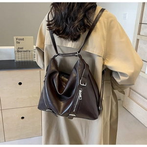 Detail view of the brown leather backpack with multiple silver zippers and glossy texture
