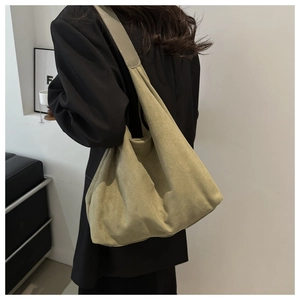 Detail of large olive green suede tote bag with wide strap on shoulder of black suit