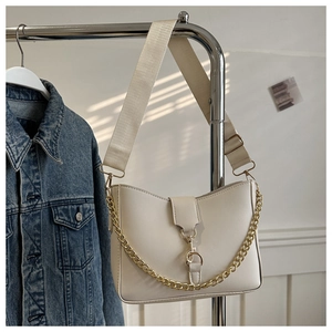 Detail of cream bucket bag with wide fabric strap and golden metal chain accessory