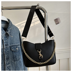 Detail of black bucket bag featuring adjustable wide strap and gold chain on denim