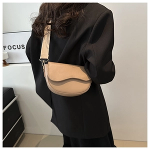 Detail of khaki saddle bag with wide fabric strap worn on model's shoulder over black suit