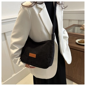 Detail of black corduroy crossbody bag with brown leather label on white suit model