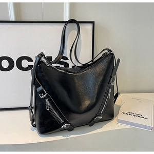 Detail of high-gloss black leather tote bag featuring silver zippers and belt buckle accents