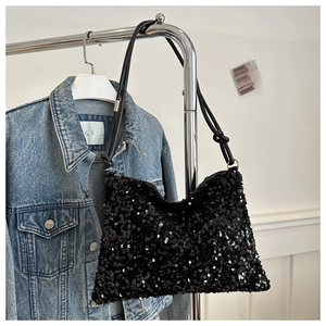 Close-up of black sequined crossbody bag with silver buckle on washed denim background