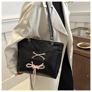 Détail du cabas en cuir noir avec ruban de laçage rose et décoration de nœud