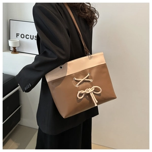 Détail d'un sac cabas bicolore avec un nœud décoratif et une texture en cuir lisse