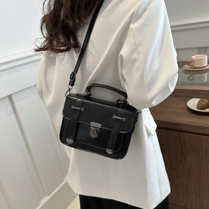 Dettaglio borsa a tracolla nera vintage con fibbie argentate su blazer bianco