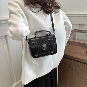 Dettaglio borsa a tracolla nera vintage con fibbia argentata indossata su blazer bianco