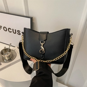 Modern black leather crossbody bag with gold chain and wide strap on minimalist table