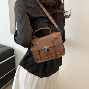 Dettaglio di una borsa a tracolla vintage in pelle marrone con fibbie e manico superiore