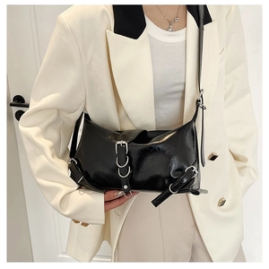 Detailed view of black glossy shoulder bag with silver buckles on white suit