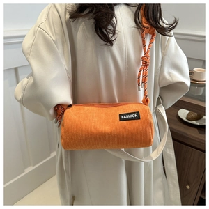 Close-up of orange corduroy barrel bag with woven strap and Fashion label details