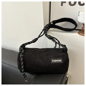 Detail of black corduroy barrel bag with FASHION label and woven rope strap on sofa