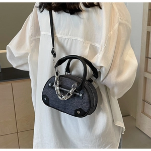 Detail of grey denim bowling bag with silver chain and black leather handles worn by a model