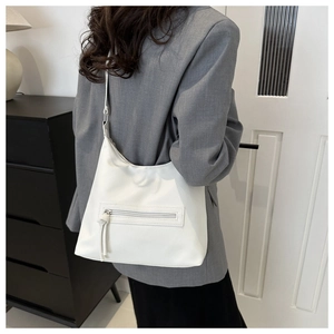 Close-up of white lychee textured shoulder bag with leather tassel detail on grey blazer