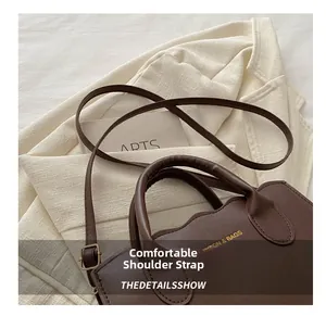 Detail of adjustable leather strap and top handle on dark brown tote bag