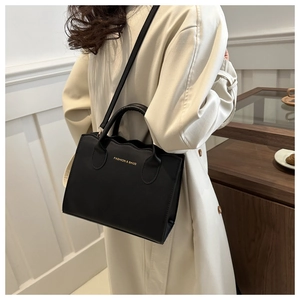 Detail of wave-edged black leather tote bag worn with a classic beige trench coat